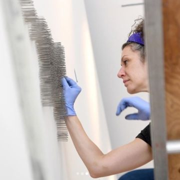 @citizentimes Shannon Sberna, an art handler and member of the installation team at the Asheville Art Museum, pushes individual pins into the wall as she works to install artist Maya Lin's Pin River-French Broad in the atrium of the new museum on July 17, 2019. The series of thousands of pins follows the map of the French Broad River from end to end. The piece will be completed at a member's event at the museum on July 26. Staff at the Asheville Art Museum are hoping to announce a day for the reopening soon. (? by staff photographer @angeliwright ).