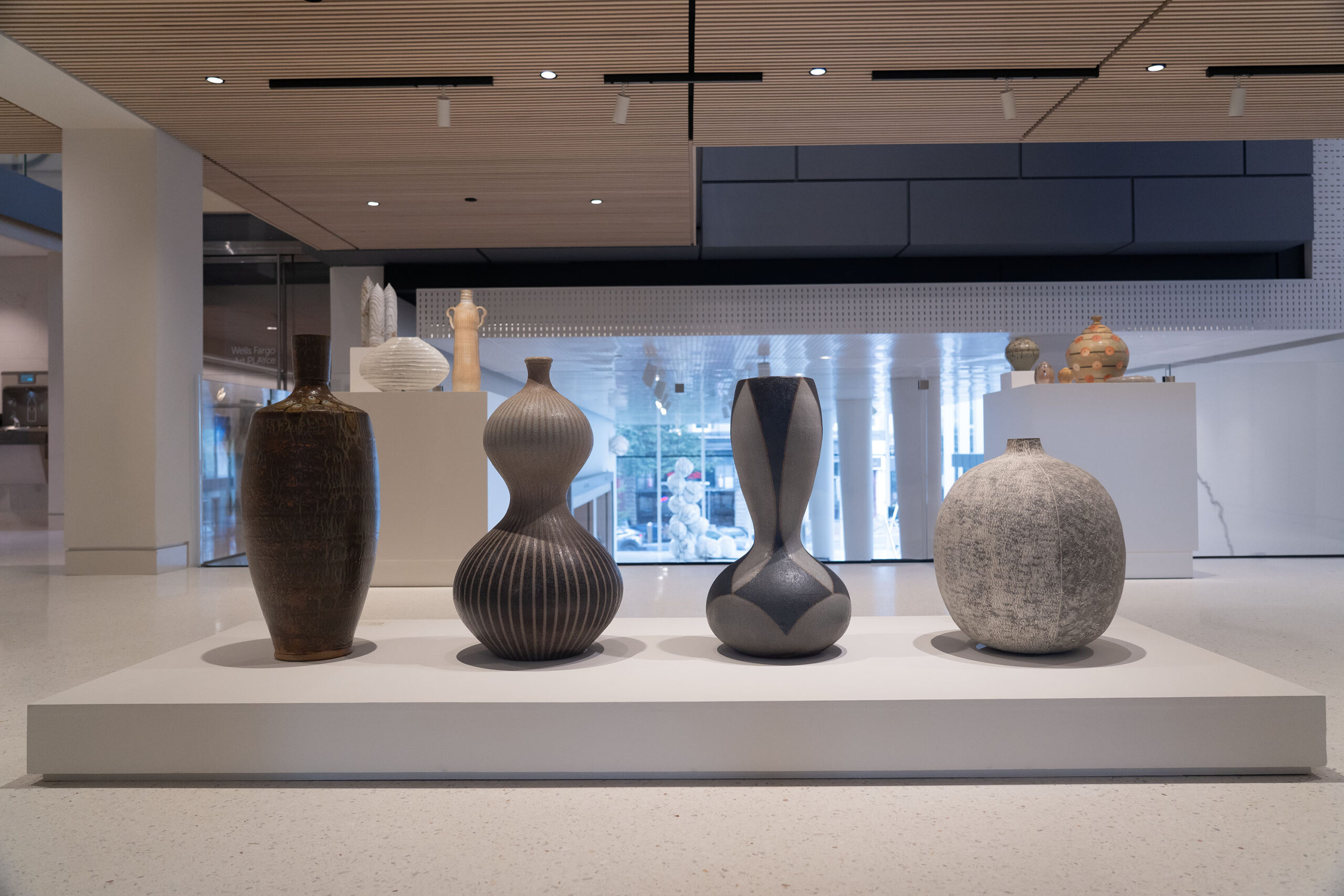 Four ceramic artworks staged in an exhibition hall with smaller pieces on display in the backround